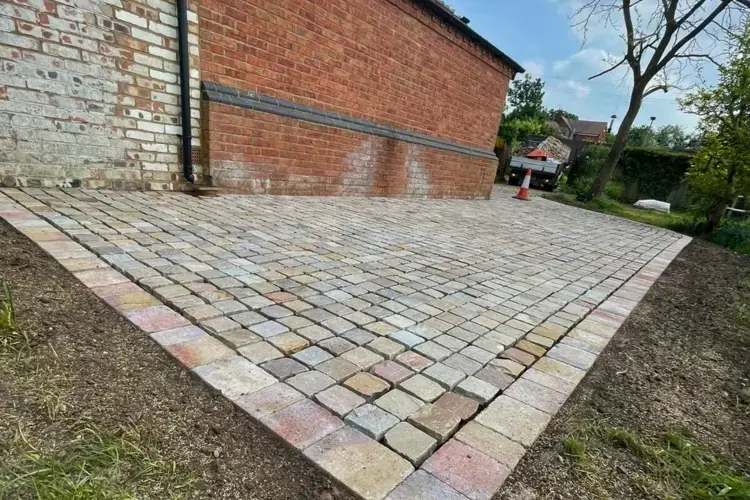 Block edge border around granite setts paving layed on this driveway landscaping project. Granite setts block paving with block edge border has been installed to extend the existing driveway around the side of a brick building.
