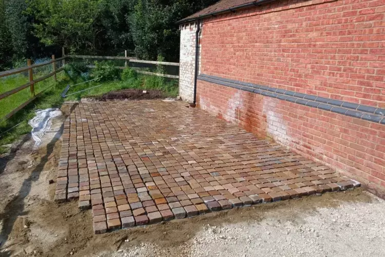 Granite setts are being layed on this driveway landscaping project. Granite setts block paving is being installed to extend the existing driveway around the side of a brick building.